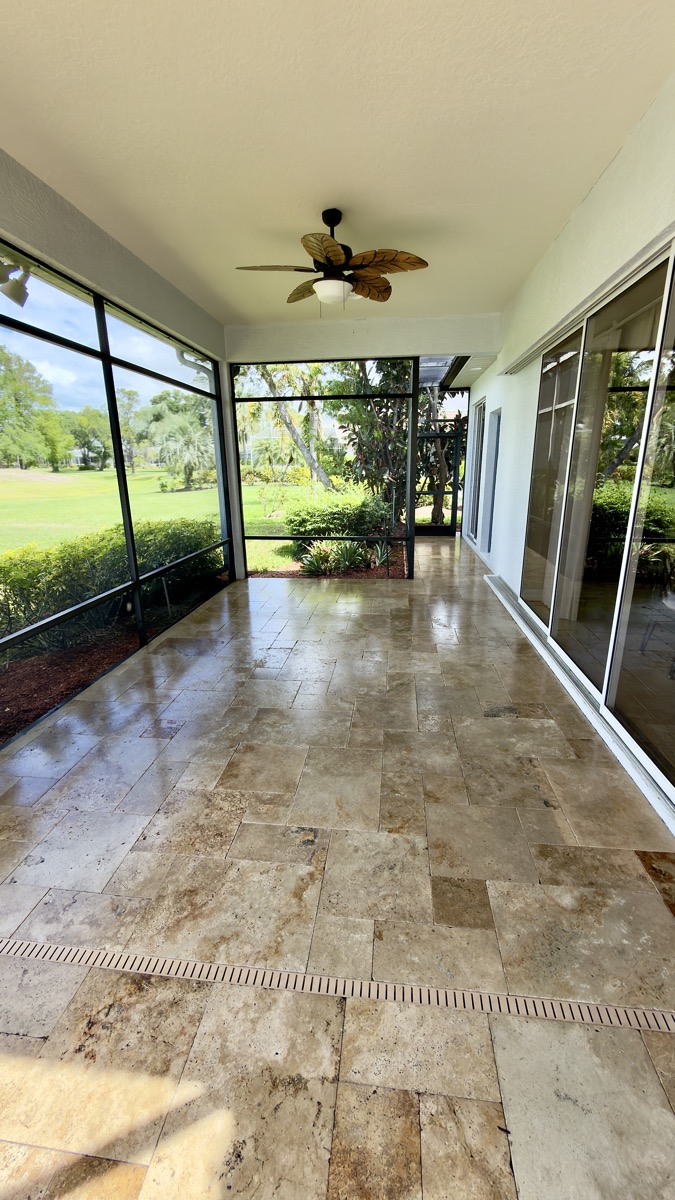 Sealed travertine lanai walkway with wet-look sheen leading past a ceiling fan