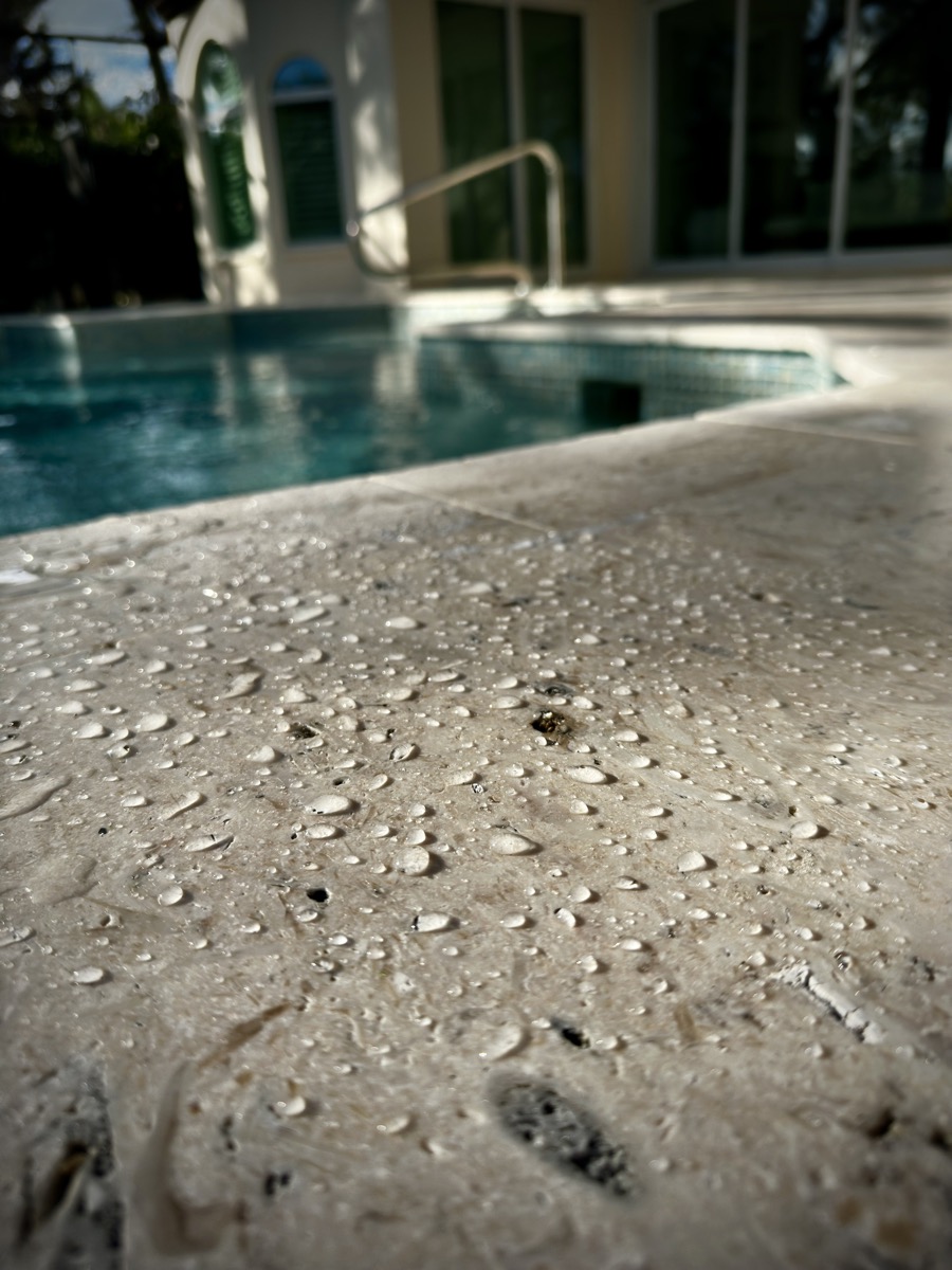 Close-up macro shot of sealed travertine pool deck texture beading water