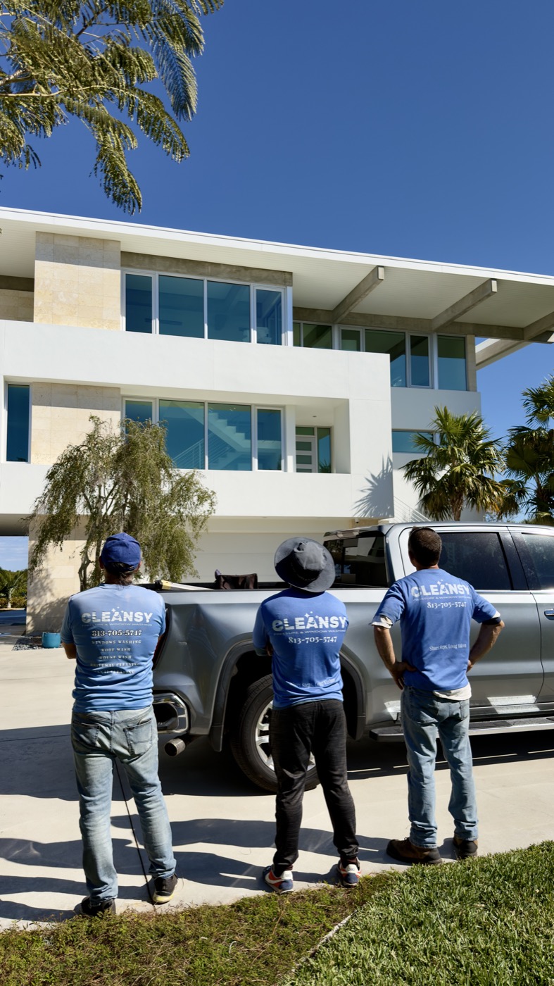 Three Cleansy crew members in branded blue shirts standing by a pickup truck in front of a modern three-story home