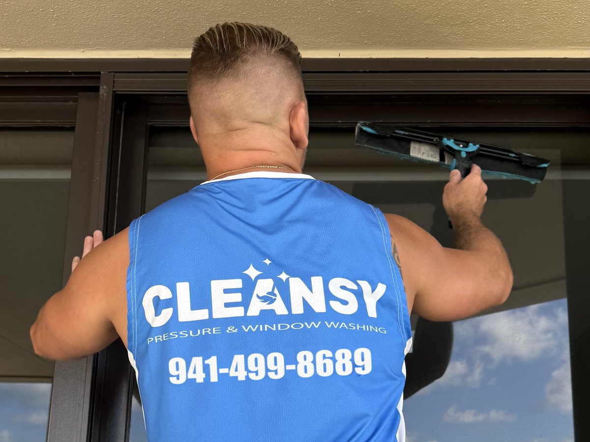 Cleansy technician in a branded blue shirt cleaning a high-rise balcony window with a squeegee