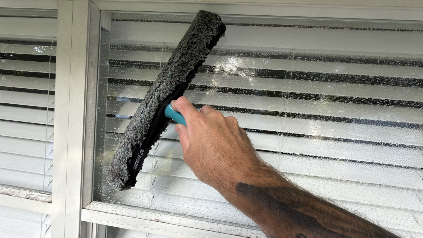 Hand washing a window with a microfiber scrubber loaded with soapy water