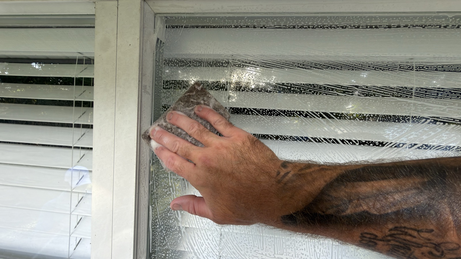 Hand rubbing a polish pad in small circles over the corner of a soapy window