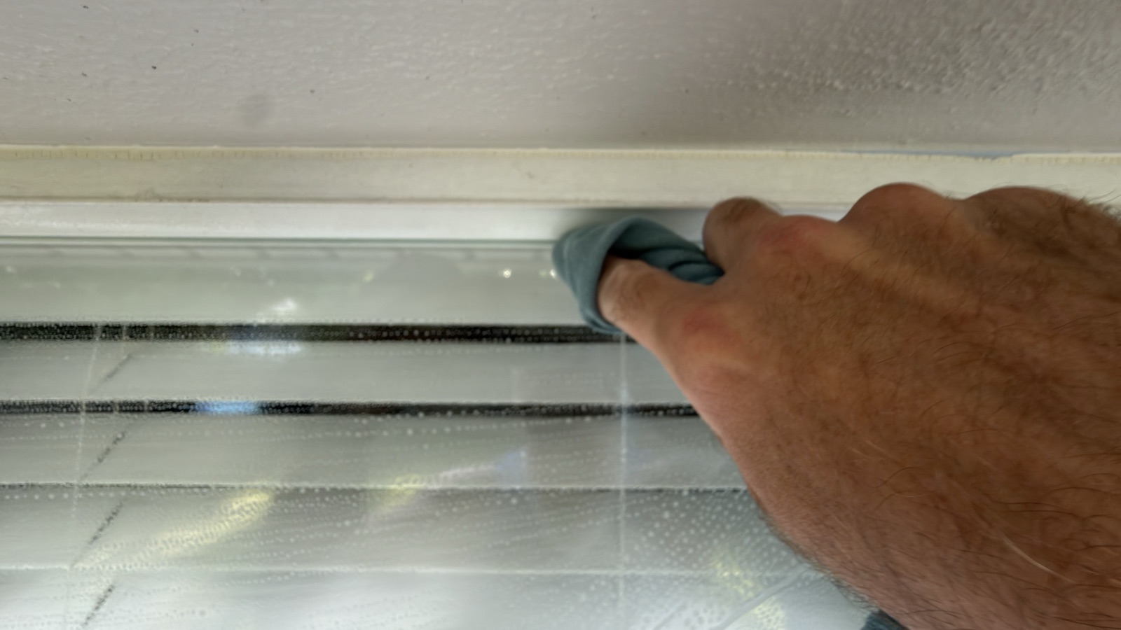 Hand wiping a thin dry line along the top edge of a soapy window with a cloth