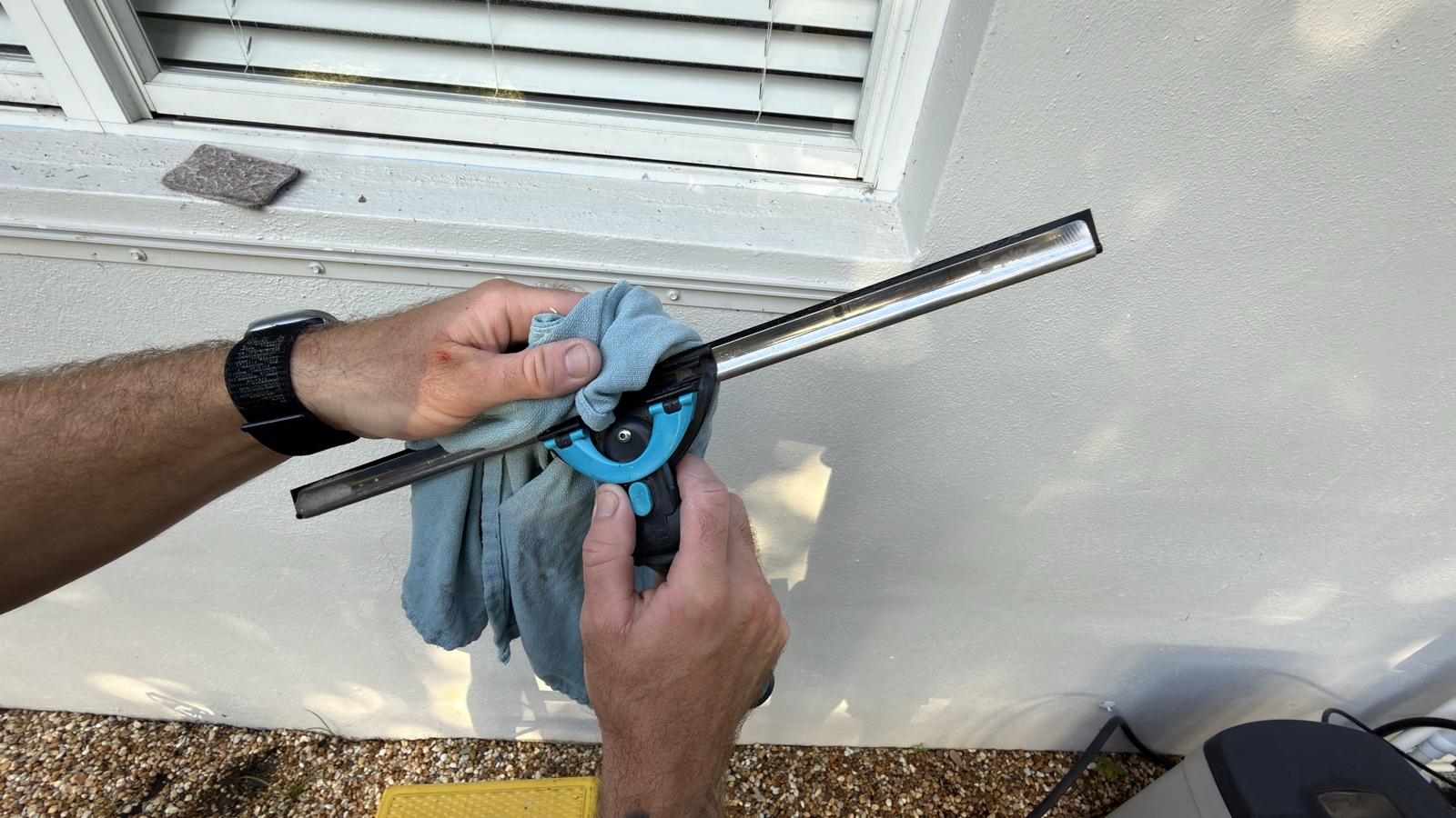 Hands wiping the rubber blade of a squeegee dry with a blue cloth