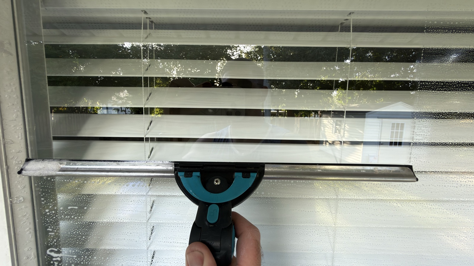 Squeegee pulled down a soapy window, leaving a clear streak-free strip of glass above the blade