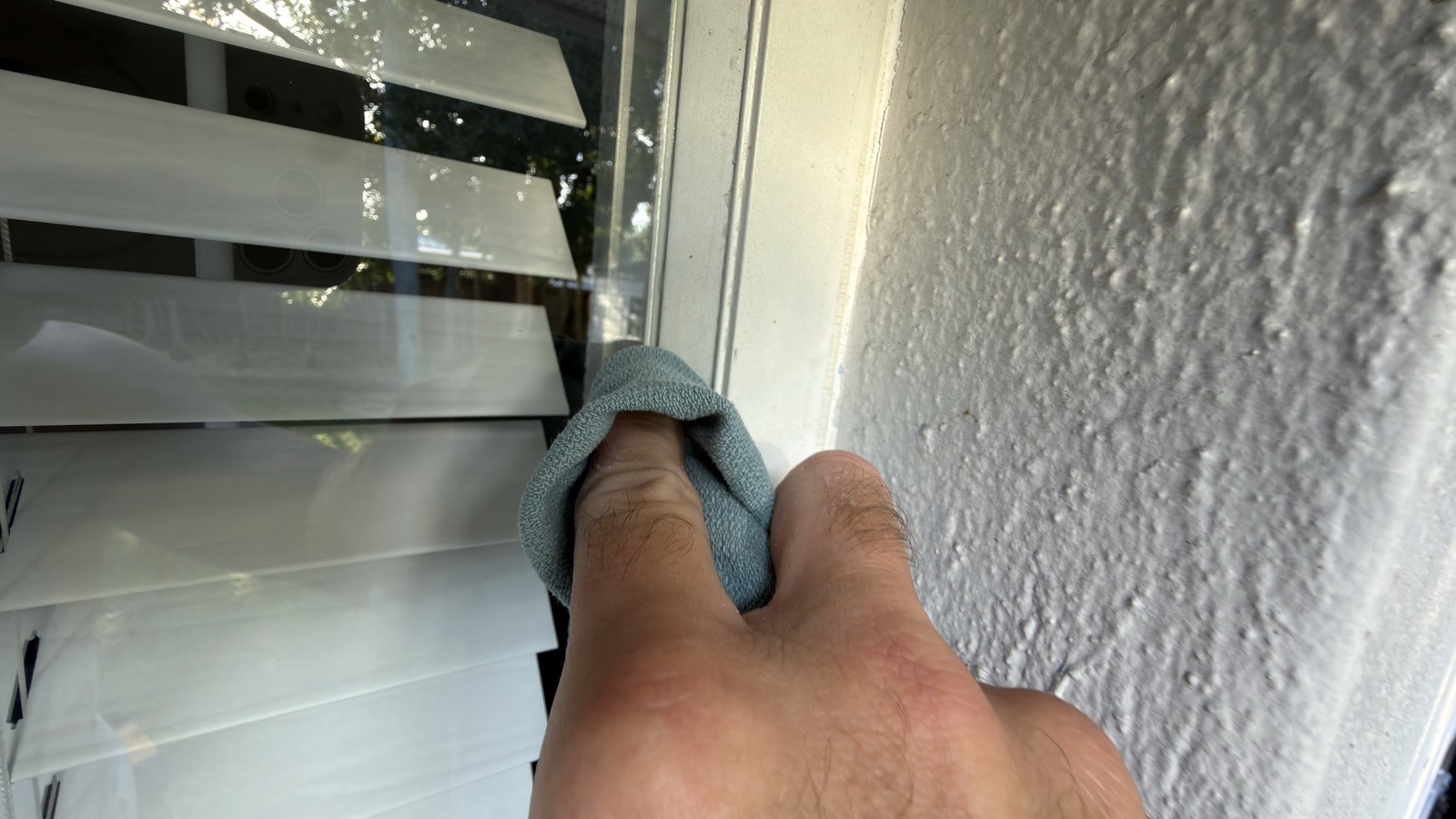 Hand wiping a window frame corner with a blue cloth to remove drips