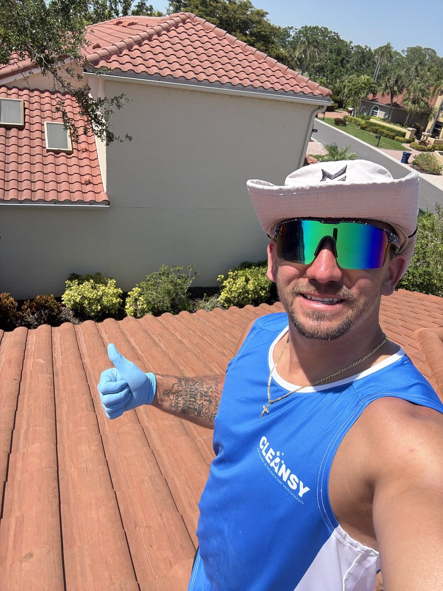 Cleansy technician giving a thumbs up while standing on a freshly soft-washed, algae-free tile roof