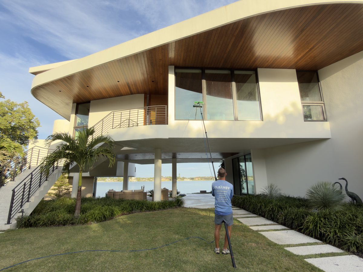 Cleansy technician cleaning the windows of a modern lakefront home with a water-fed pole