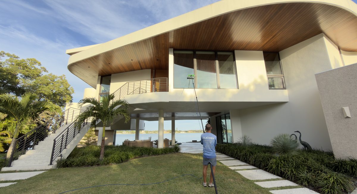 Cleansy technician cleaning the windows of a modern lakefront home with a water-fed pole