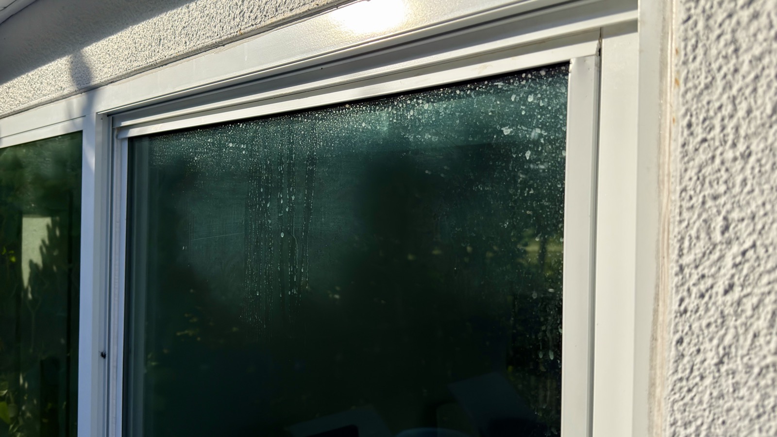 Window glass with a heavy band of white hard water spotting across the top, typical of sprinkler overspray