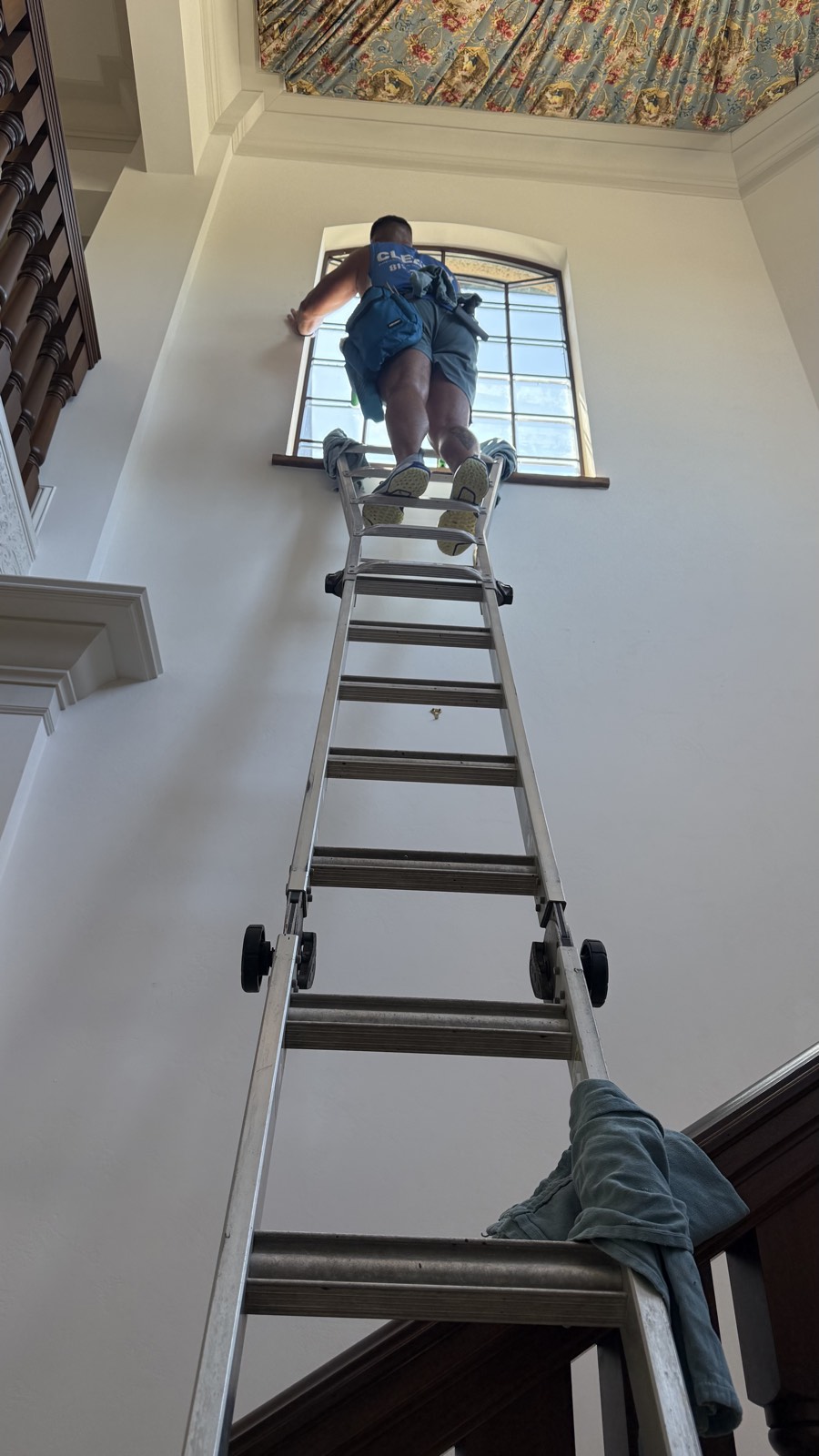 Cleansy technician on an extension ladder reaching a tall interior window
