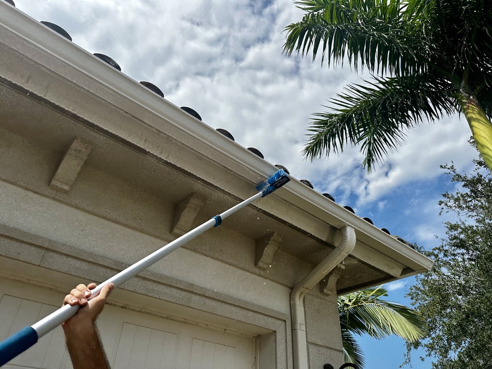 Technician brushing a soffit and gutter clean with a palm tree in the background